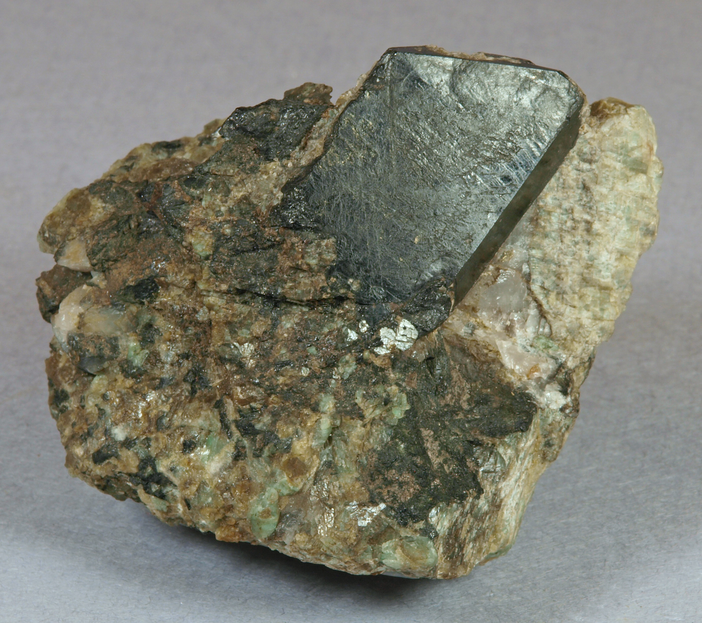 Sharply formed, bladed allanite crystal, 4 cm long, matrix of medium-grained, bluish-green microcline and quartz