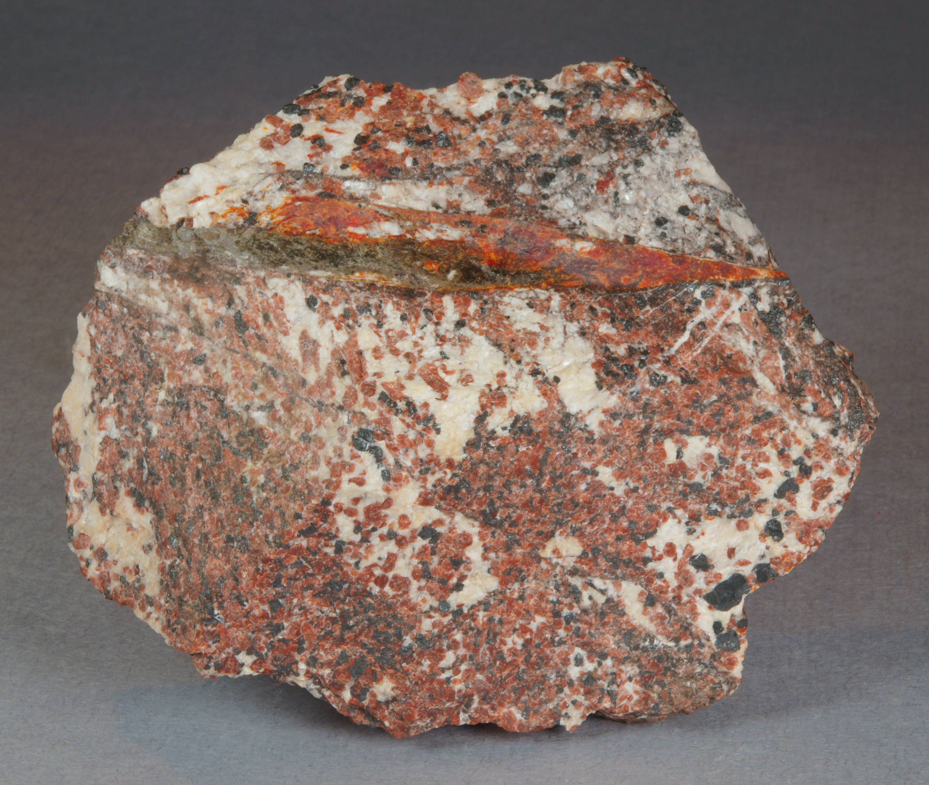 Dark olive green to (locally) dark brown magnussonite and orange-red zincite